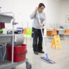 A person mops a floor with a wet floor sign nearby.